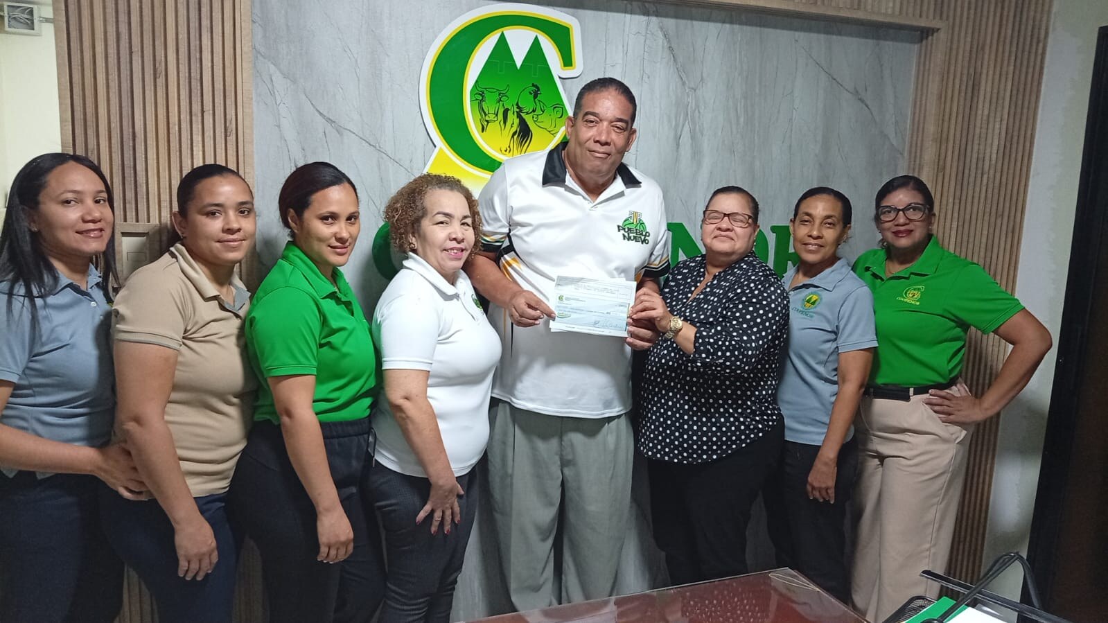 Tony Reyes recibe el aporte de Damary de la Cruz, administradora de COOPENOR, junto a empleadas de la cooperativa